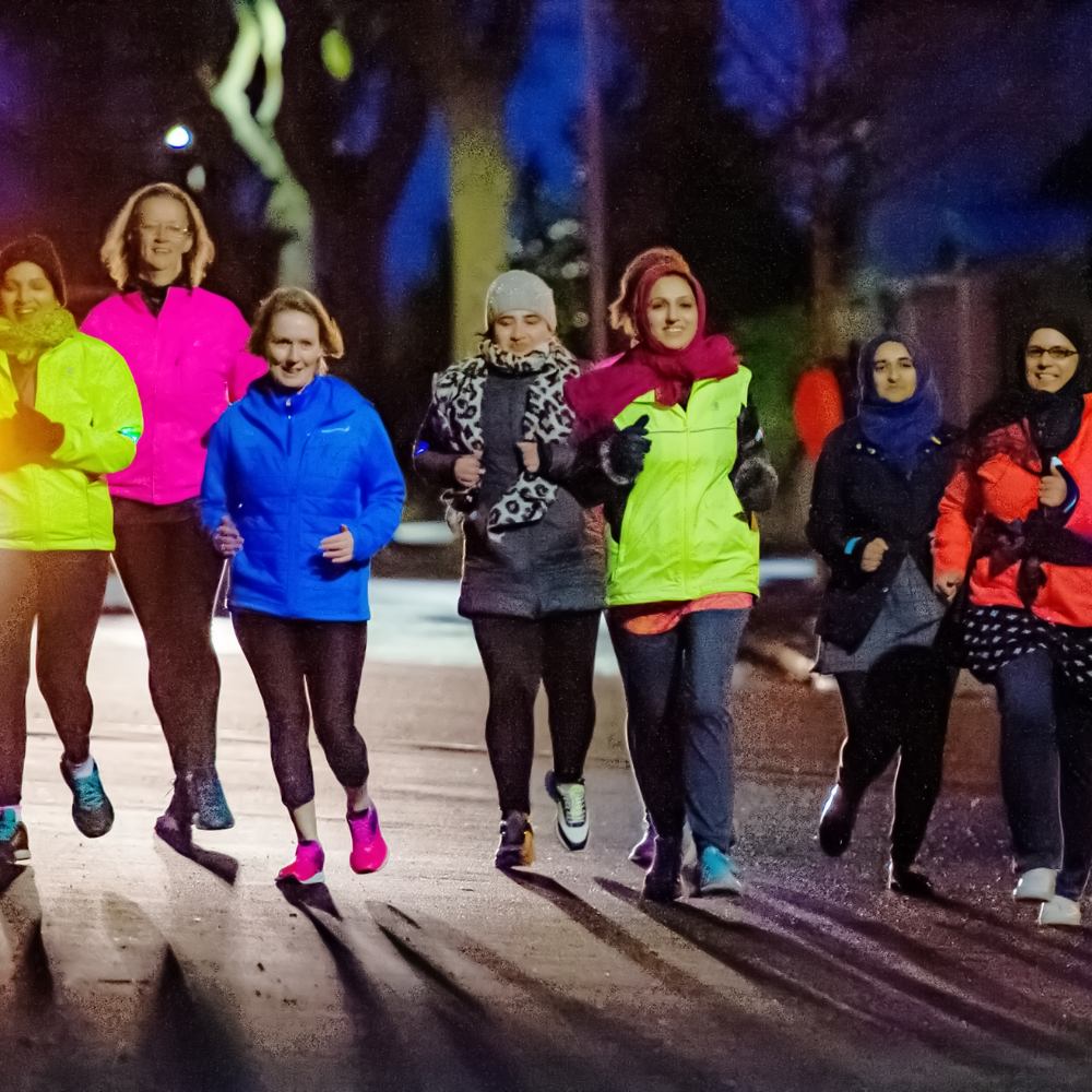 Women running at night wearing bright reflective clothes. The runner in the foreground is wearing a dupatta headdress