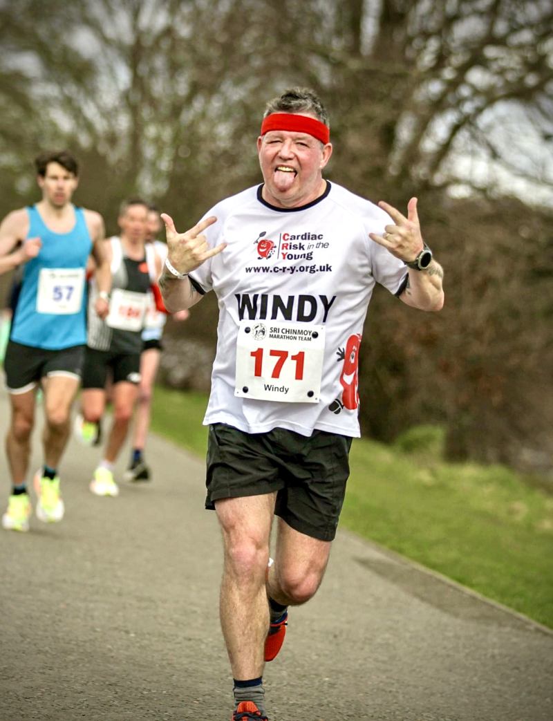 People in a running event one man in front holding his arms out smiling to the camera