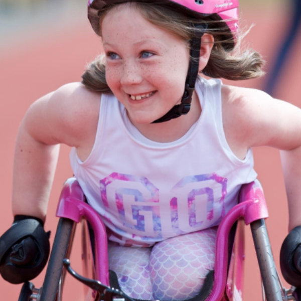 A young girl smiling while racing in a racing wheelchair