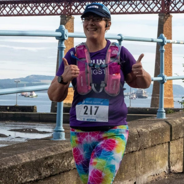 A woman running smiling with her thumbs up